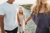 Серйозна дівчина робить сумне обличчя, ходячи з батьками на пляжі — стокове фото