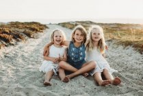 Retrato de três jovens irmãs abraçando e sorrindo na areia — Fotografia de Stock