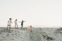 Vier junge Schwestern spielen und laufen im Sand bei Sonnenuntergang am Strand — Stockfoto
