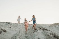 Quatro jovens irmãs correndo na areia ao pôr-do-sol da praia — Fotografia de Stock