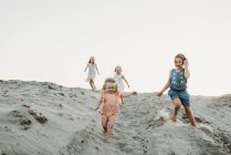 Чотири молодих сестри бігають і грають в пісок на заході сонця на пляжі — стокове фото