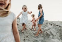 Чотири молодих сестри бігають і грають в пісок на заході сонця на пляжі — стокове фото
