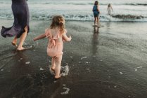 Vue de derrière de la jeune famille marchant vers l'océan au coucher du soleil — Photo de stock