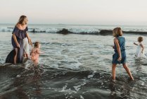 Сильна мати з чотирма доньками, які грають в океані на заході сонця — стокове фото