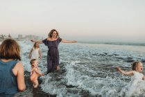 Сильна мати з чотирма доньками, які грають в океані на заході сонця — стокове фото