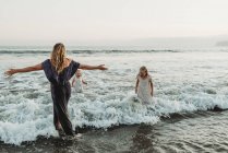 Mãe e duas meninas salpicando no oceano ao pôr do sol — Fotografia de Stock