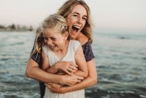 Mãe abraçando jovem com sardas no oceano rindo — Fotografia de Stock