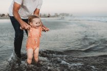 Niña chapoteando en el océano con su padre al atardecer - foto de stock