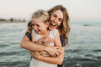 Мать обнимает молодую девушку с веснушками в океане, смеясь — стоковое фото