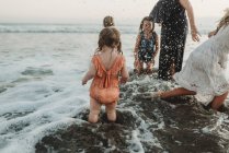 Jovem menina criança salpicando com irmãs e mãe na praia ao entardecer — Fotografia de Stock