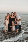 Portait de jovem família com cabelo molhado em pé no oceano ao pôr do sol — Fotografia de Stock