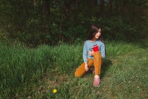 Спокійна дівчина сидить у високій траві, дивлячись з книгою на руках — стокове фото