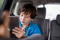 Un garçon assis dans un siège auto lors d'un voyage en voiture regardant une tablette — Photo de stock