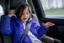 Una bambina ascolta musica con le cuffie in macchina durante un viaggio in auto — Foto stock