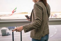 Женщина в аэропорту с помощью смартфона с самолетом на заднем плане — стоковое фото