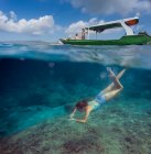 Молодая женщина сноркелинг рядом с лодкой в океане, вид под водой — стоковое фото