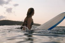 Surfeuse dans l'océan au coucher du soleil — Photo de stock