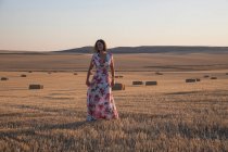 Femme debout dans le champ de blé au coucher du soleil — Photo de stock
