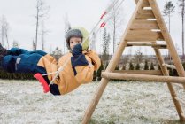 Close up de um menino balançando em um balanço fora no inverno — Fotografia de Stock