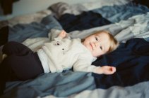 Niedliches kleines Baby blickt in die Kamera, während es auf dem Bett seiner Eltern liegt — Stockfoto