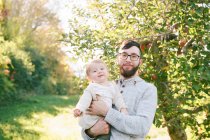 A proud father and his 6 month old daughter next to an apple tree. — Stock Photo