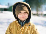 Un niño feliz sonriendo sobre la nieve en su patio trasero. - foto de stock