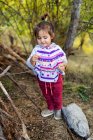 Улыбающаяся маленькая девочка с деревянной палкой, стоящей в лесу — стоковое фото