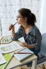 Millennial chica dibuja fabulosas imágenes en papel mientras se sienta en casa - foto de stock