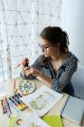 Millennial fille dessine des images fabuleuses sur papier tout en étant assis à la maison — Photo de stock