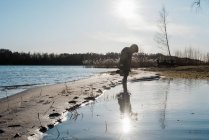 Junge spielt im Winter am sonnigen Strand im Wasser — Stockfoto