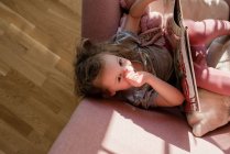 Areal view of young girl sat on a chair looking up at home reading — Stock Photo