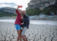 Casal tirando uma selfie na beira de um lago durante uma viagem. — Fotografia de Stock