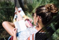 Жінка в сонцезахисних окулярах читає книгу, що лежить на гамаку . — стокове фото