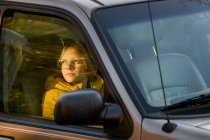 Хлопчик сидить у машині, дивлячись на вікно воріт, що встановлює сонце — стокове фото