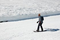 Сноубордист бежит по склону горнолыжного курорта в смешной шляпе. Зимний спорт и отдых, досуг на открытом воздухе — стоковое фото