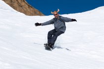 Snowboarder running down the slope in ski resort with a funny hat. — Stock Photo