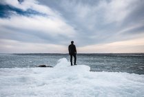 Homem em pé em uma costa gelada de um lago olhando para a distância. — Fotografia de Stock
