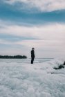Homem em pé em uma costa gelada de um lago olhando para a distância. — Fotografia de Stock