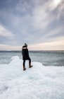 Mujer de pie en la costa helada de un lago mirando a la distancia. - foto de stock
