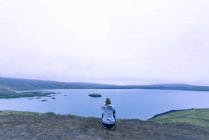 Женщина, сидящая и фотографирующая озеро в высокогорье Исландии на закате — стоковое фото