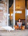 Жінка сидить у дверях будинку і годує домашніх птахів — стокове фото