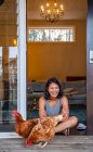 Женщина сидит в дверях дома и кормит домашних птиц — стоковое фото