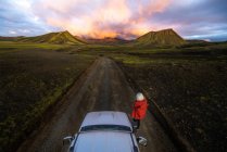 Fotógrafo tomando fotos de la puesta de sol en las montañas al lado del coche - foto de stock