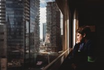 Entre garçon regardant par la fenêtre à de hauts bâtiments de la ville à l'extérieur. — Photo de stock