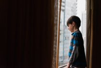 Молодий хлопчик дивиться вікно на високі будівлі міста зовні . — стокове фото