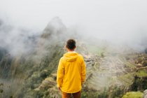 Um homem com uma jaqueta amarela está de pé perto de ruínas de Machu Picchu, Peru — Fotografia de Stock