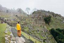 Un homme vêtu d'une veste jaune se tient près des ruines du Machu Picchu, Pérou — Photo de stock