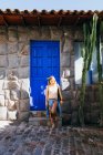 Uma jovem mulher está parada perto de uma porta azul velha em Cusco, Peru — Fotografia de Stock