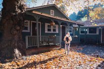 A woman with a child is standing near a house on yellow leaves — Stock Photo
