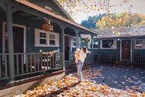 Una donna con un bambino è in piedi vicino a una casa su foglie gialle — Foto stock